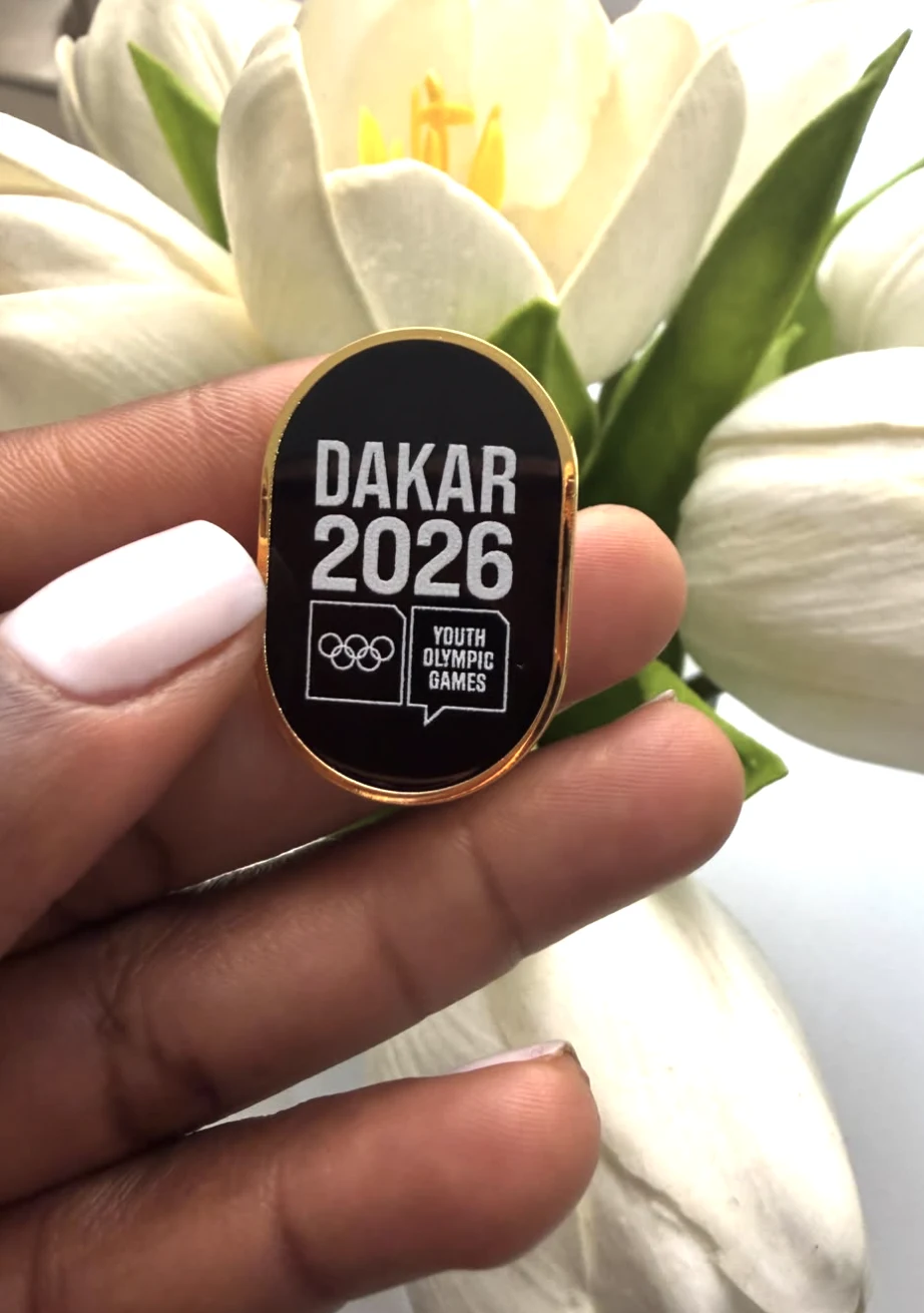Insigne Dakar 2026 tenu devant des fleurs blanches